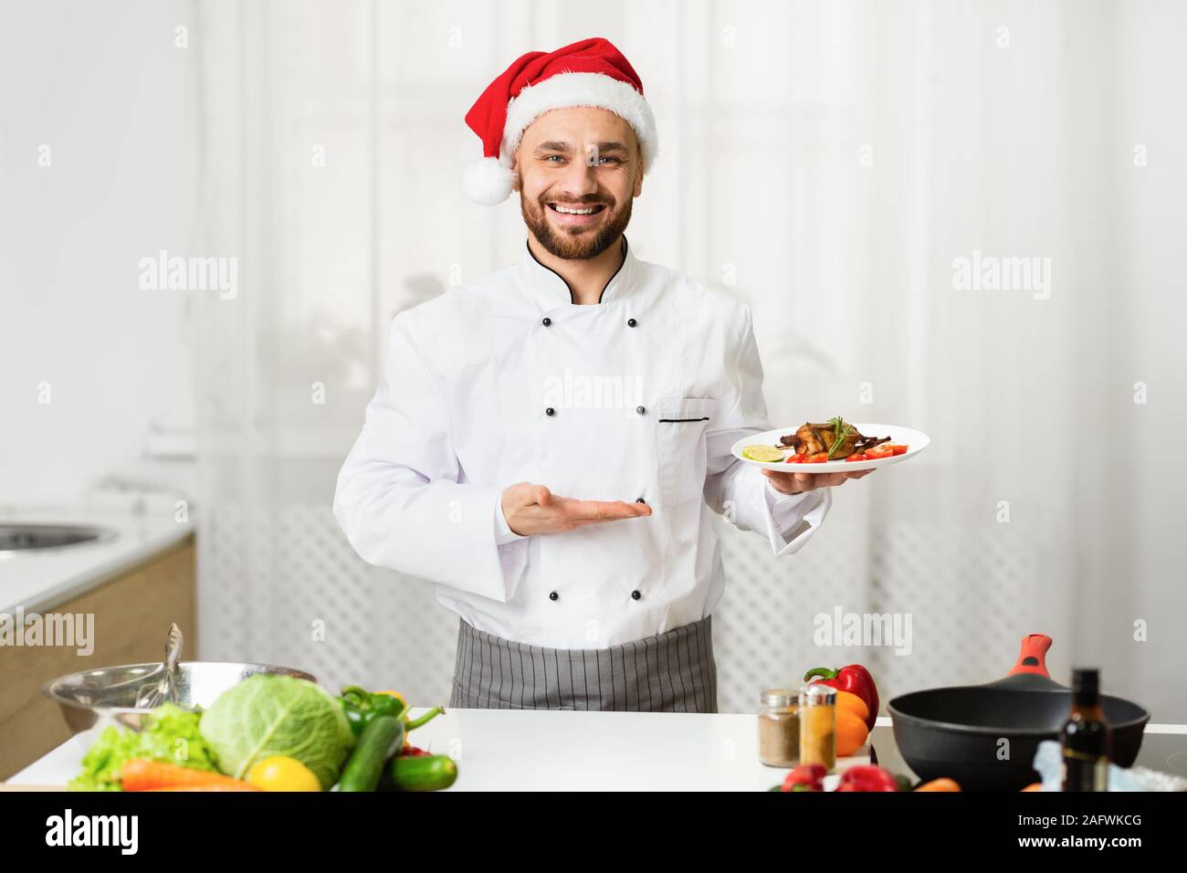 Chef Man In Santa Hat Presenting Dish Standing In Kitchen Stock Photo