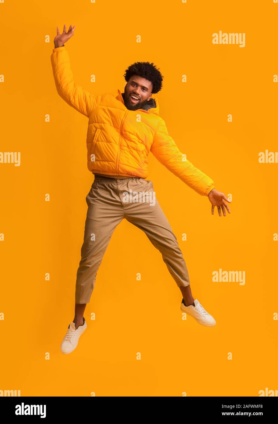 Joyful black man in winter jacket happily jumping up Stock Photo