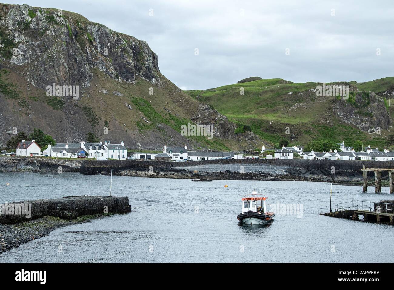 Looking back towards the harbour of Ellenabeich, a small village on the isle of Seil  from Easdale Island with the small ferry boat approaching Stock Photo