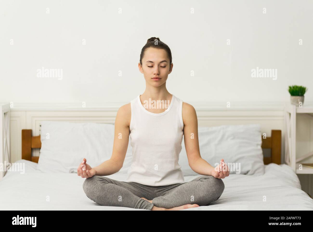 Meditation. Millennial woman sitting in lotus position on bed Stock Photo