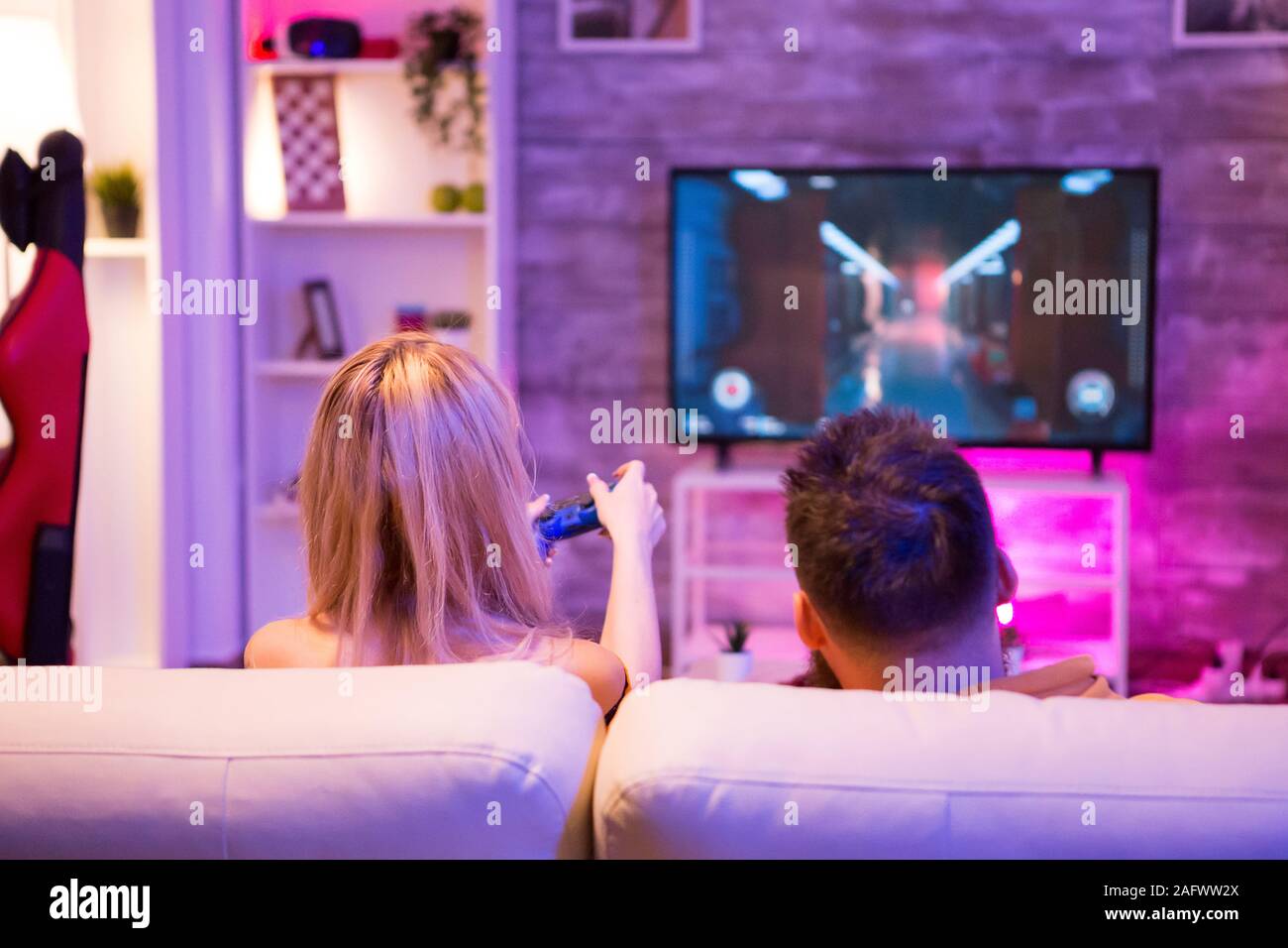 Back view of young couple relaxing playing online shooter games on