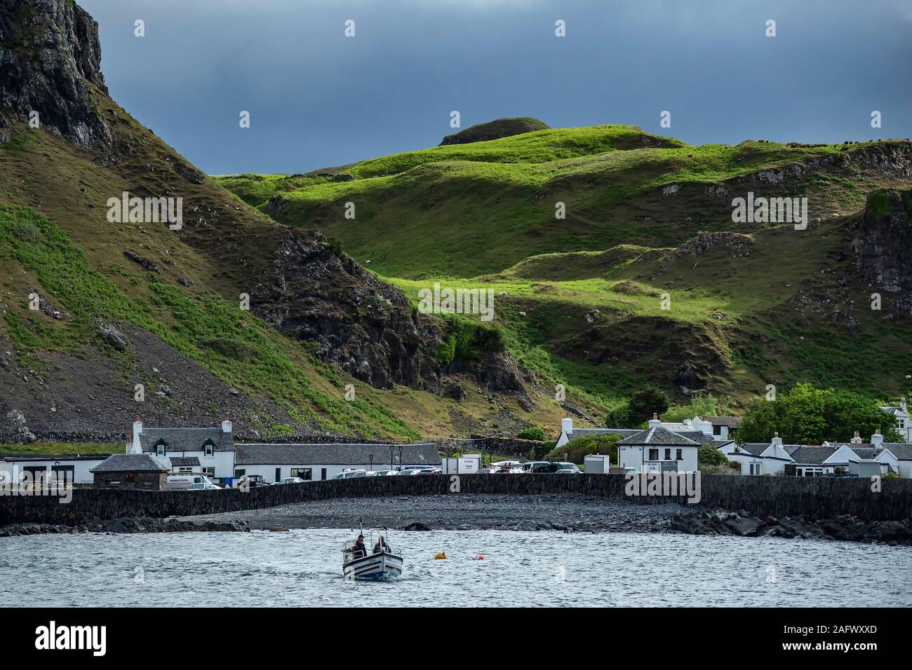 Looking back towards the harbour of Ellenabeich, a small village on the isle of Seil  from Easdale Island, with the small ferry boat approaching. Stock Photo