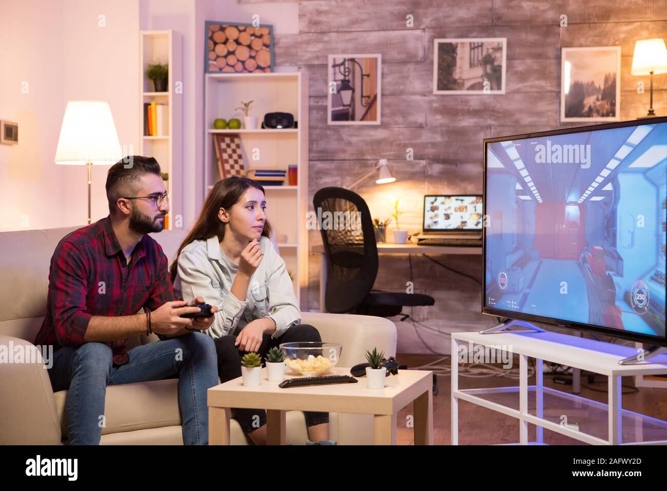 Man sitting on sofa next to his girlfriend and playing video games on television. Stock Photo