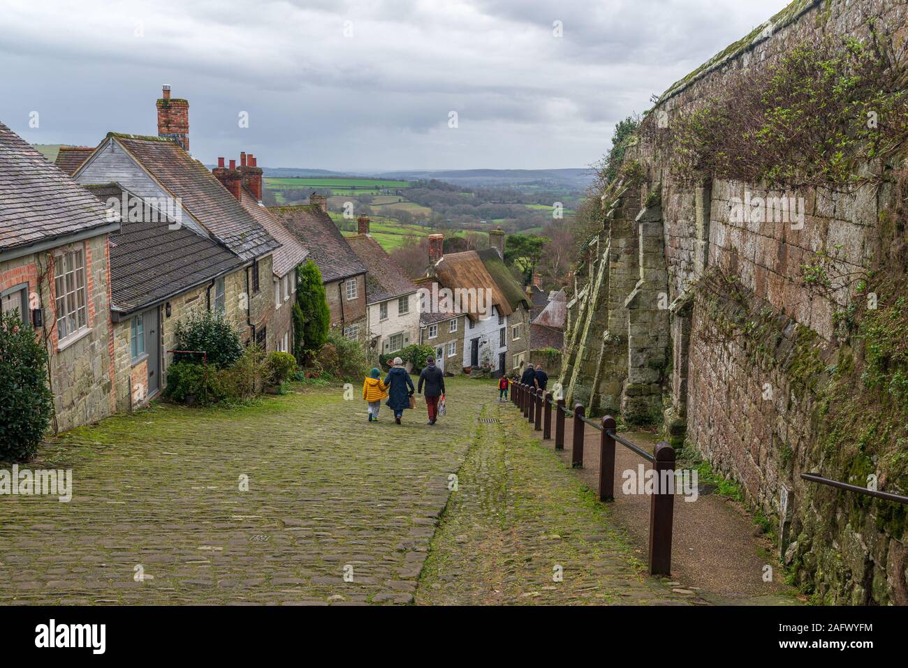 People walking down the steep cobbled street with thatched cottages, Gold Hill, Shaftesbury, Dorset, UK in December Stock Photo