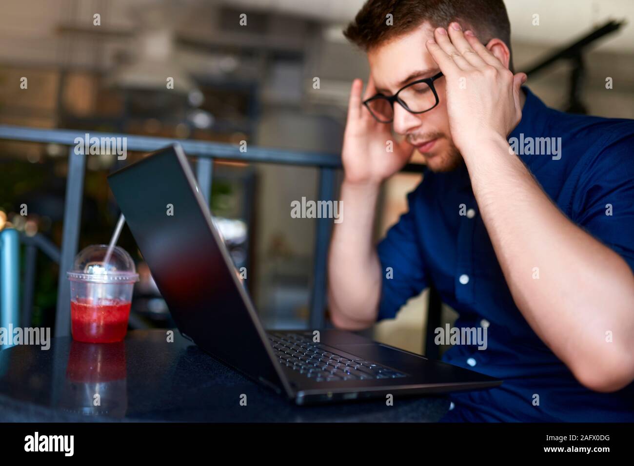 Serious frustrated businessman with closed eyes suffering from headache migraine at workplace, massaging temples. Feeling tired. Chronic work stress. Stock Photo