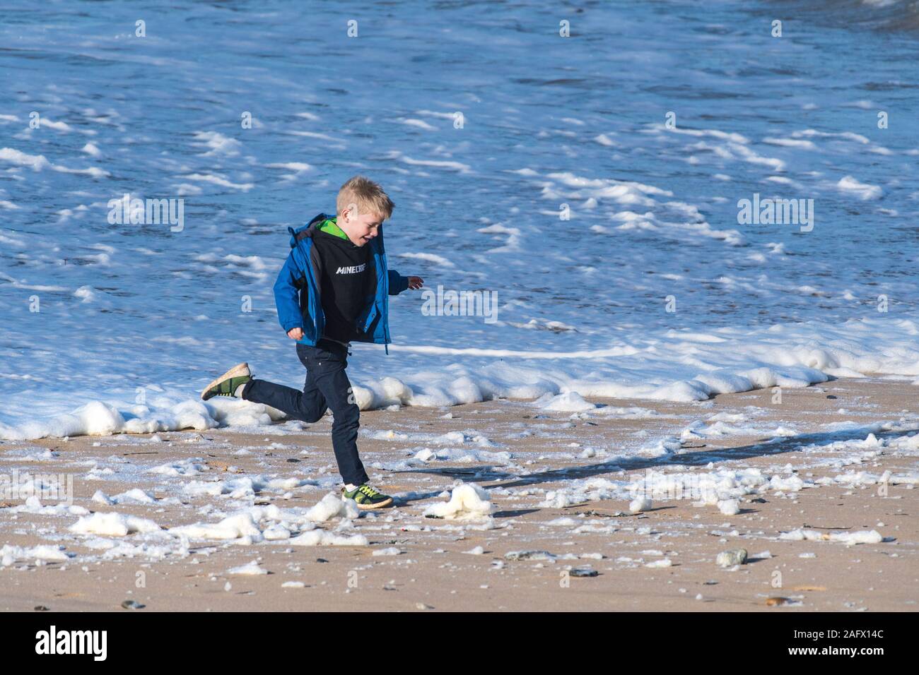 A young boy having fun running through the spume blown onto Fistral Beach in Newquay in Cornwall. Stock Photo