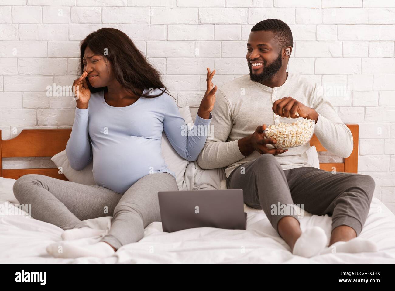 Joyful man eating popcorn while pregnant woman turning away Stock Photo