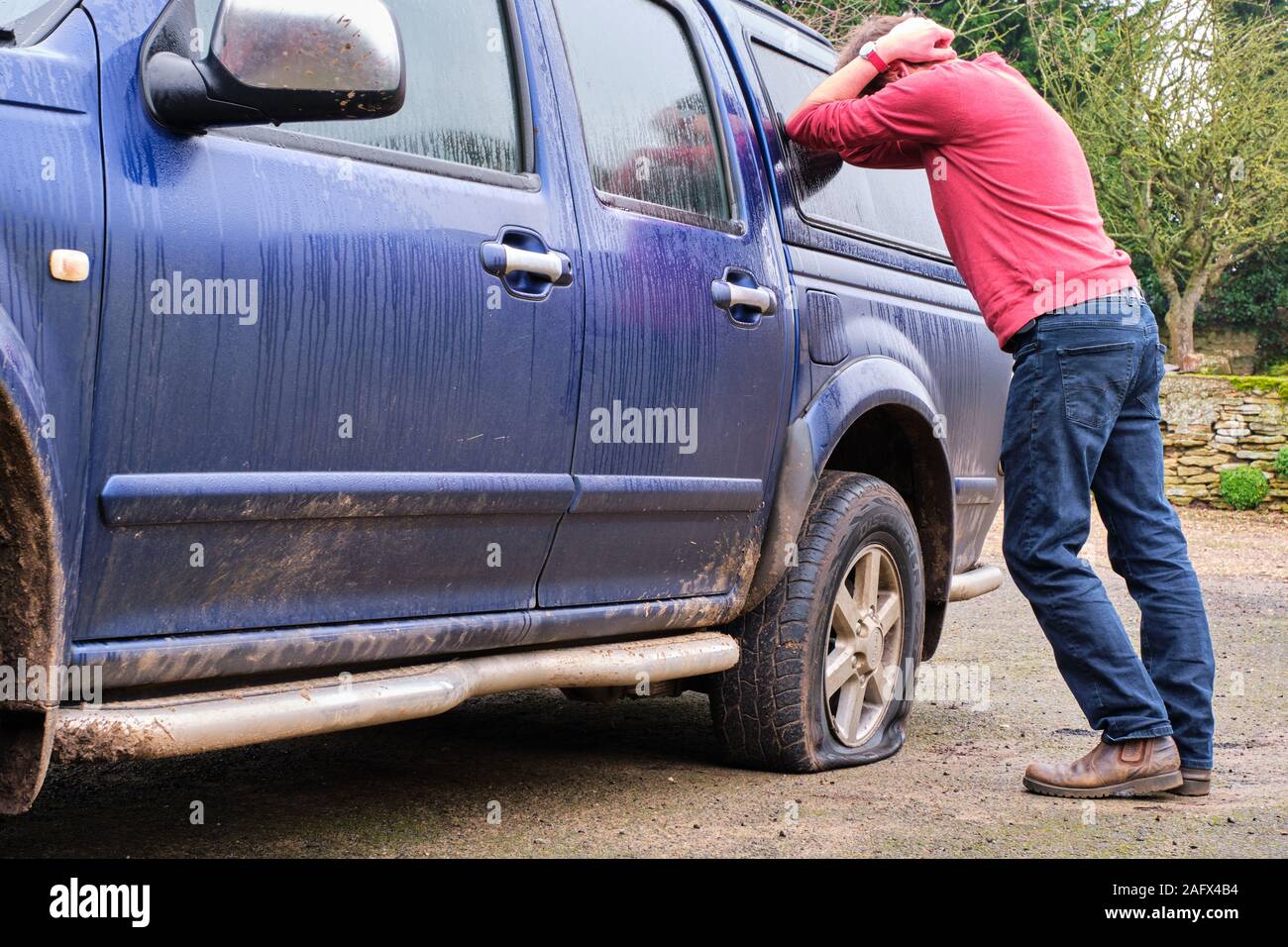 Man leaning on car head in hands in despair at finding 4x4 with flat tyre. Late for work puncture Stock Photo