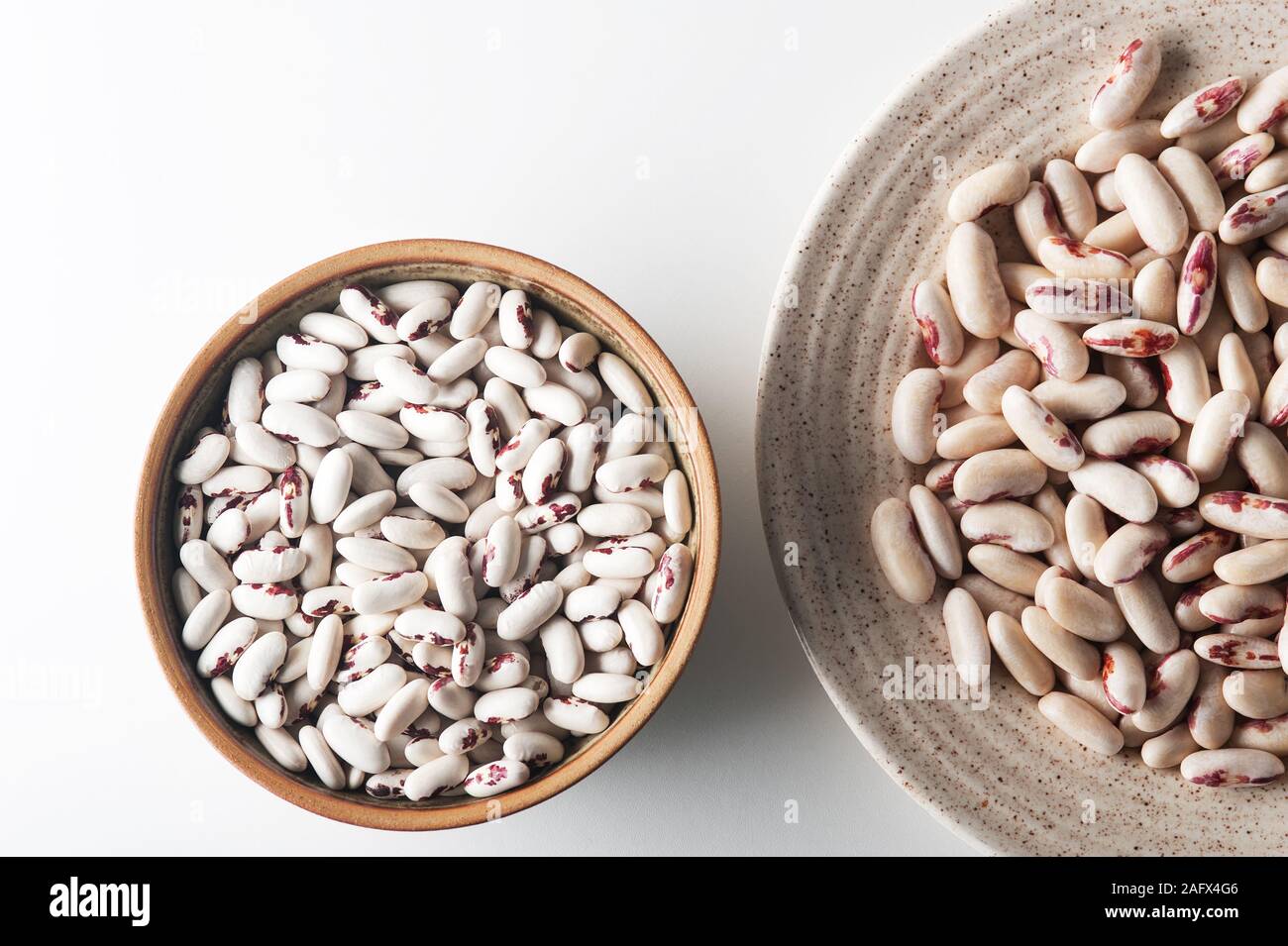 Dried white beans and soaking beans in the bowls over white background