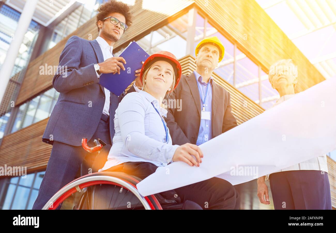 Disabled woman in a wheelchair as an architect with blueprint next to engineers and business people Stock Photo