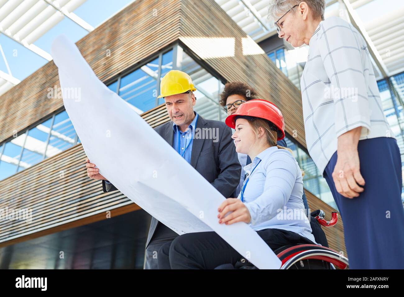 An engineering team with a blueprint and an architect in a wheelchair are planning an urban development project Stock Photo