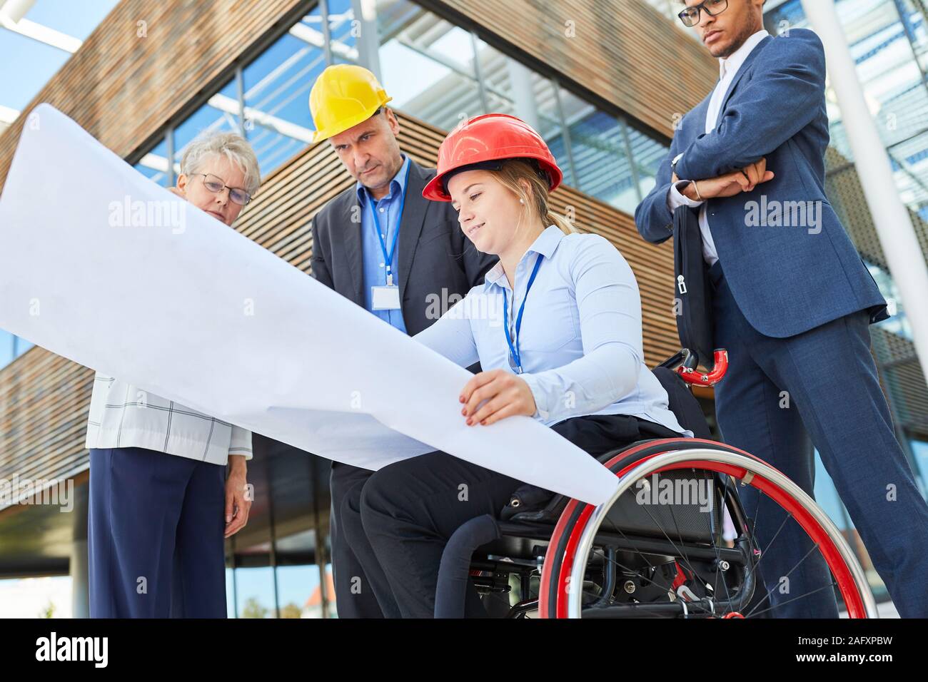 Disabled woman as an architect in a wheelchair with blueprint together with engineers Stock Photo