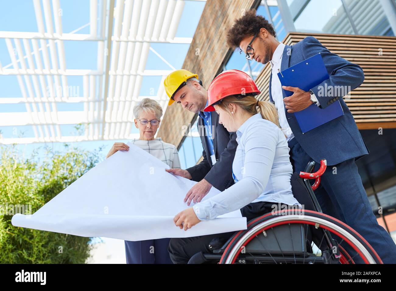 Disabled architect in a wheelchair and engineers look at the blueprint together Stock Photo