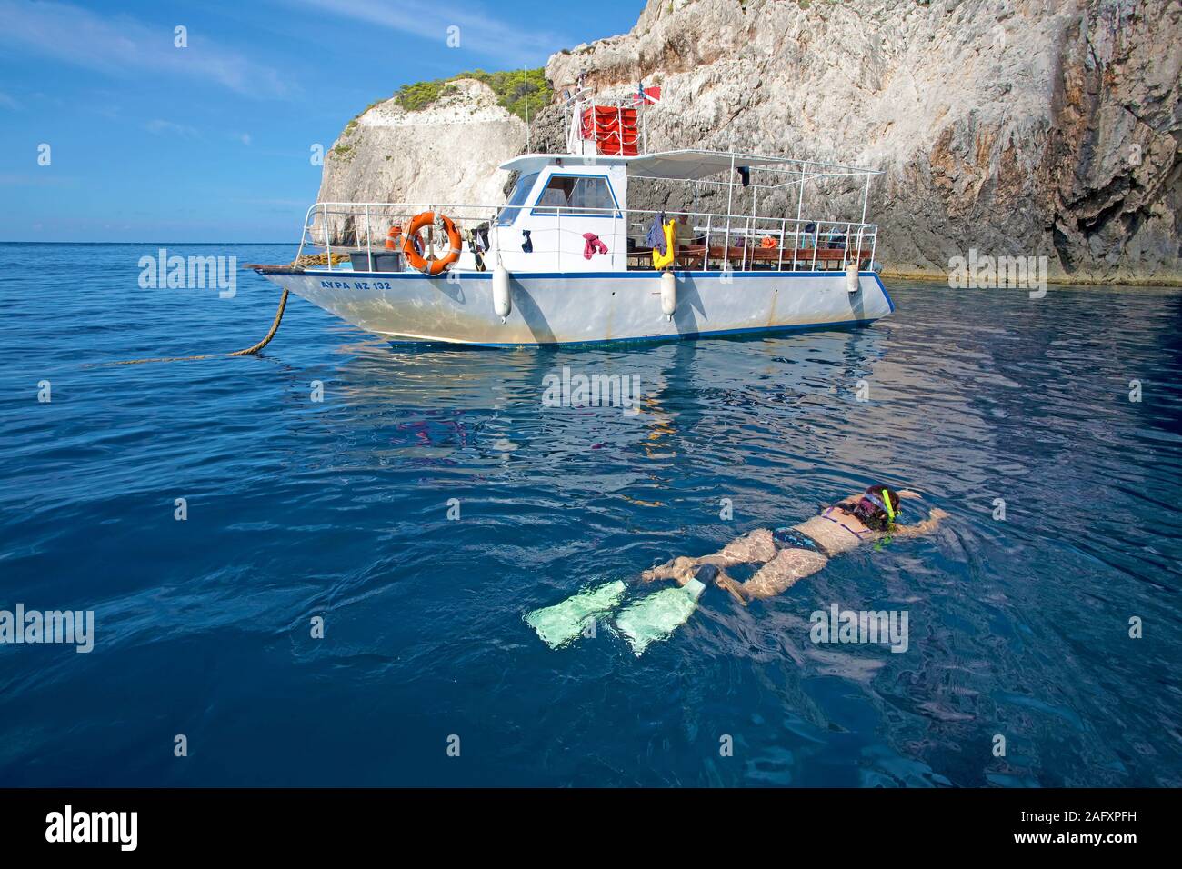 Snorkeller (woman) at dive boat, rocky coast of Zakynthos island, Greece Stock Photo