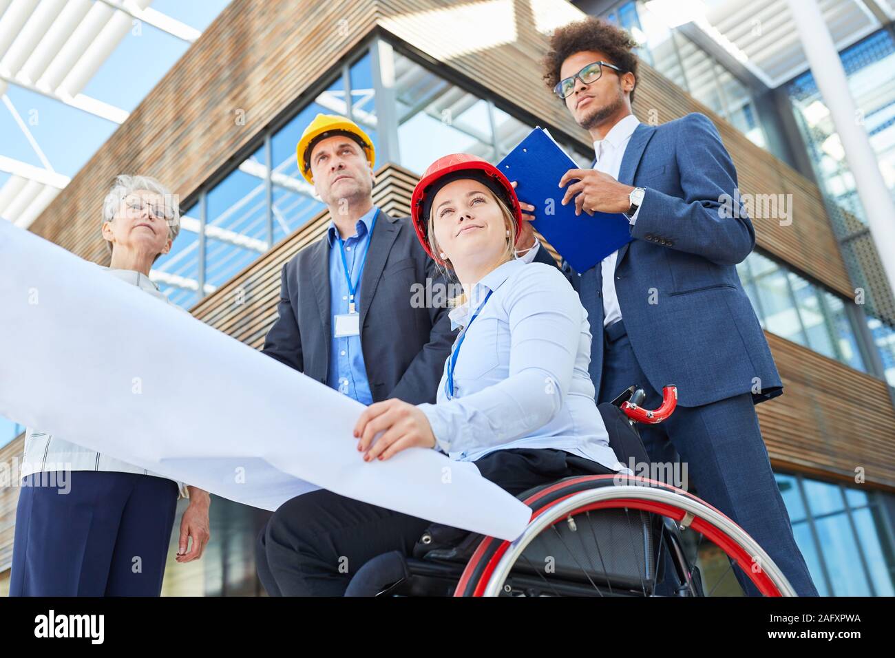 Woman as an architect in a wheelchair with blueprint next to engineers for an office Stock Photo