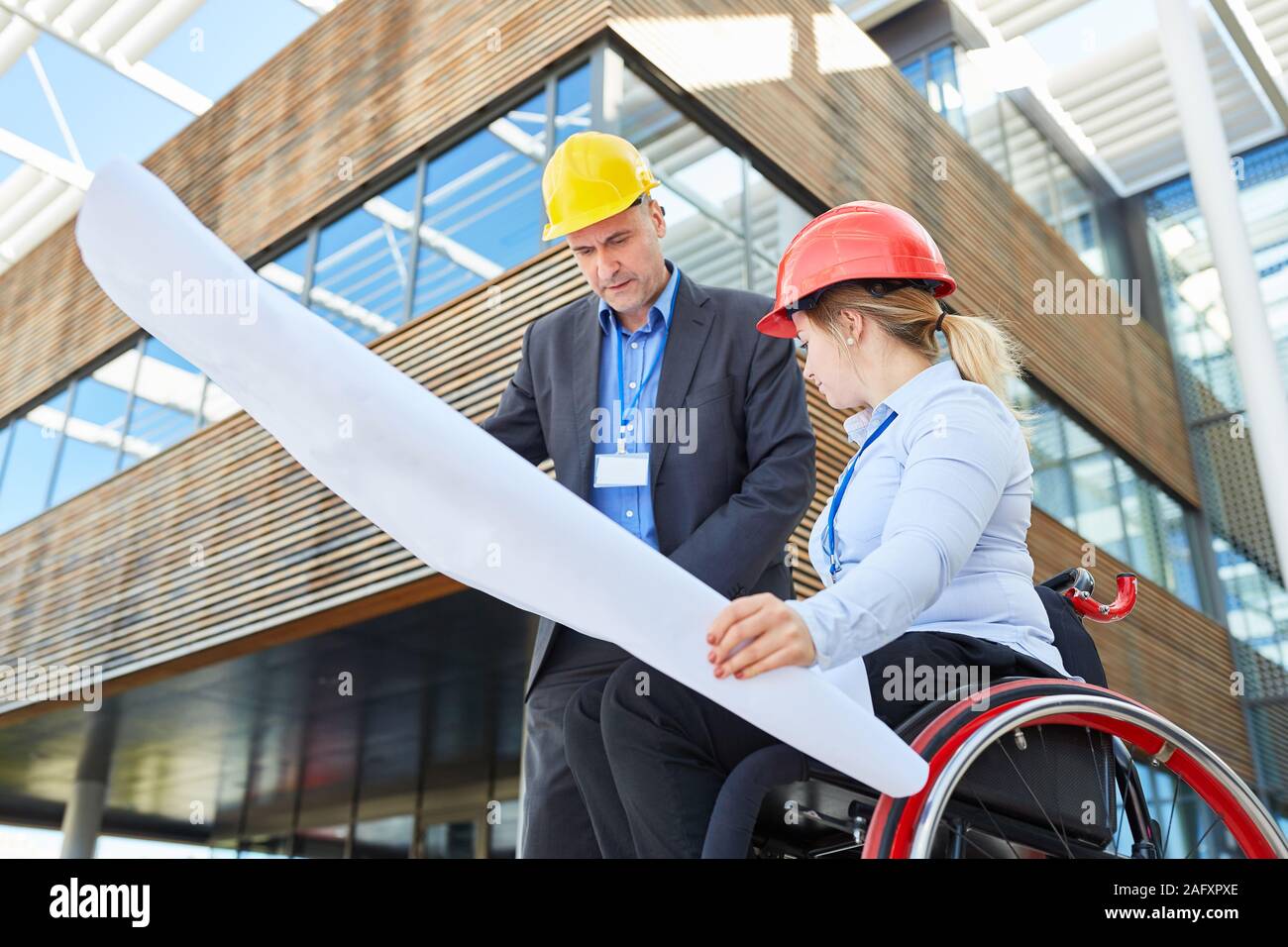 Engineer with blueprint and woman as an architect or site manager in a wheelchair for inclusion Stock Photo