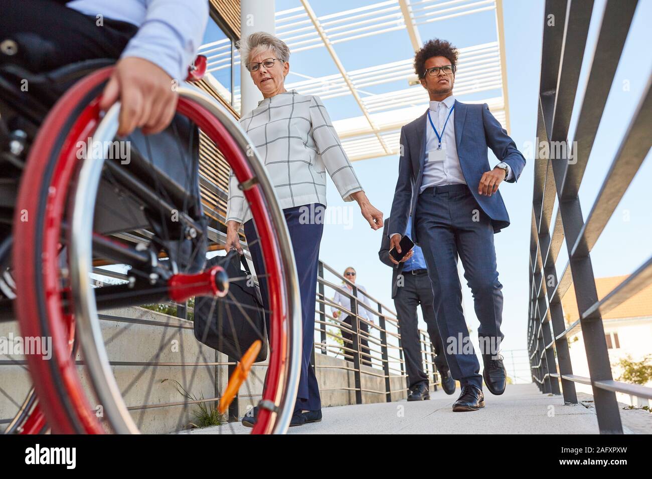 Business people and wheelchair users on a ramp in front of the office ...