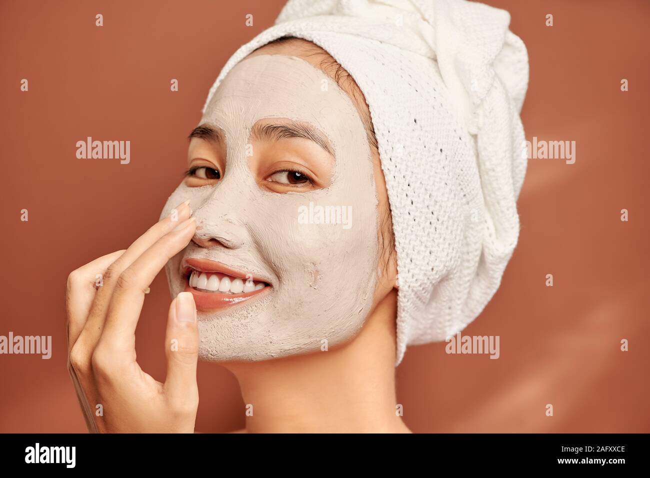 Beautiful Asian woman applying facial mask on her face. Skin care and treatment, spa, natural beauty and cosmetology concept. Stock Photo