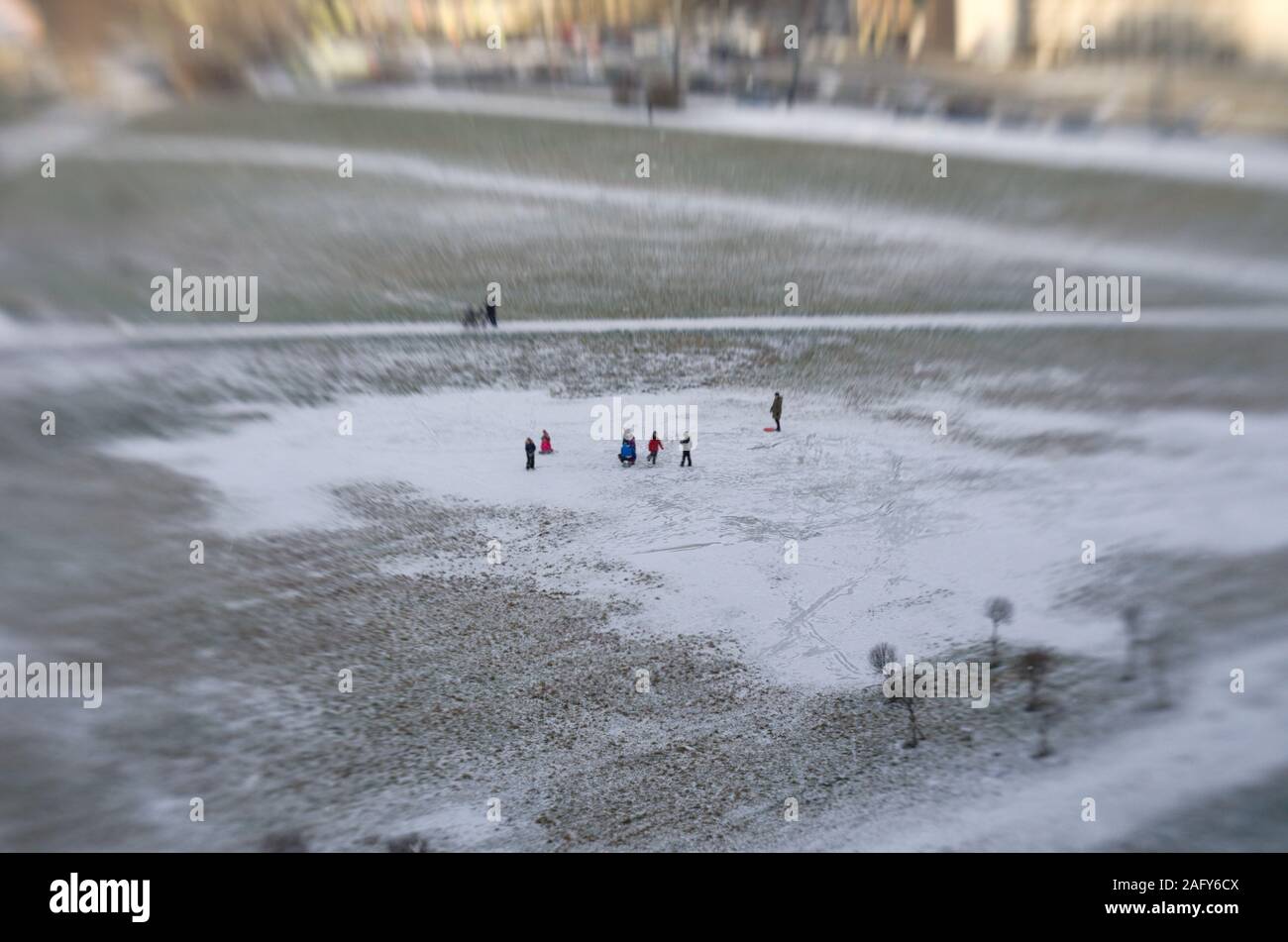 Tilt shift view from afar of unidentified adults and children walking in a large puddle covered with ice and snow in the city square Stock Photo