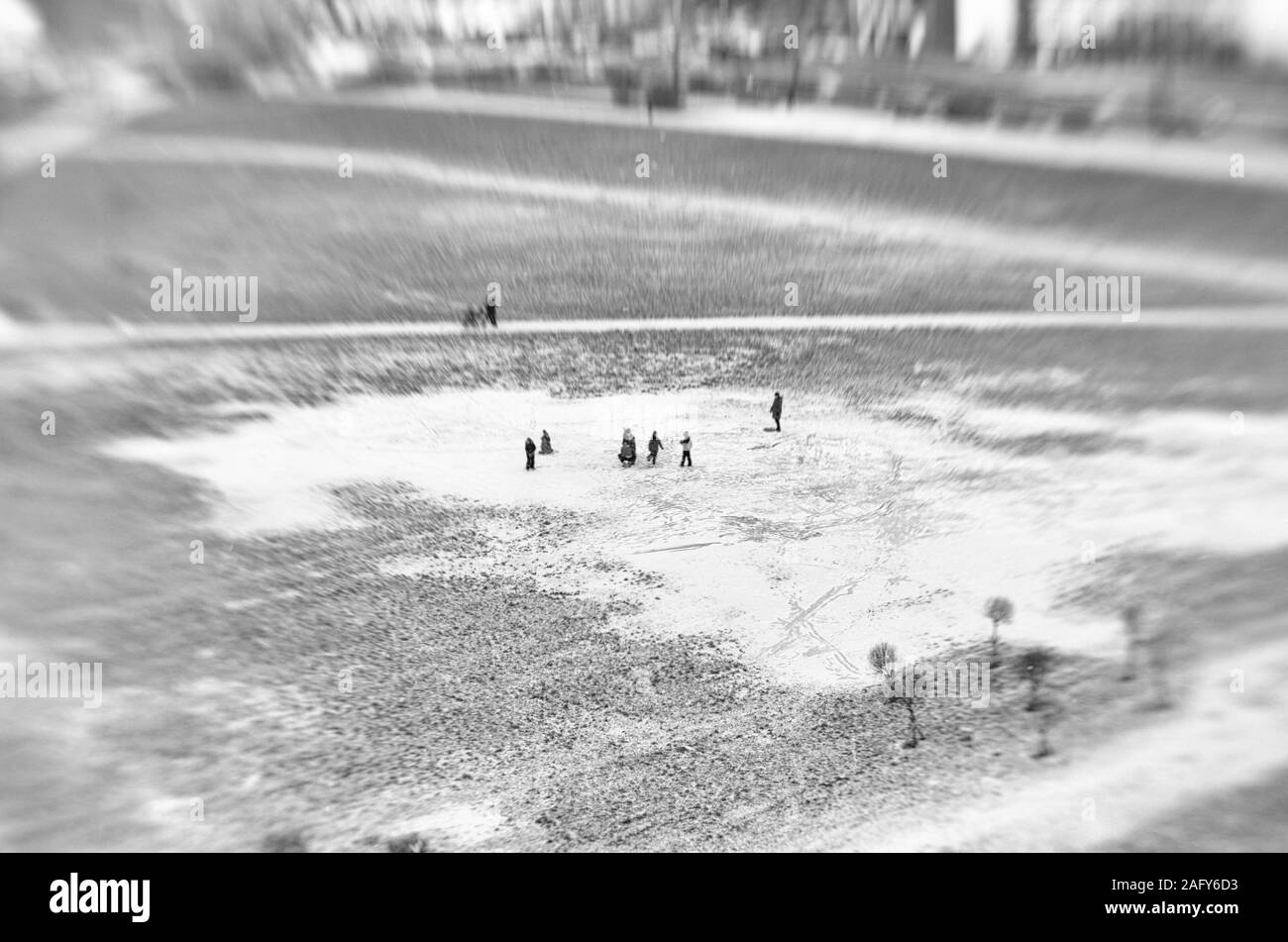 Unusual view from afar of unidentified adults and children walking in a large puddle covered with ice and snow in the city square in the black and whi Stock Photo