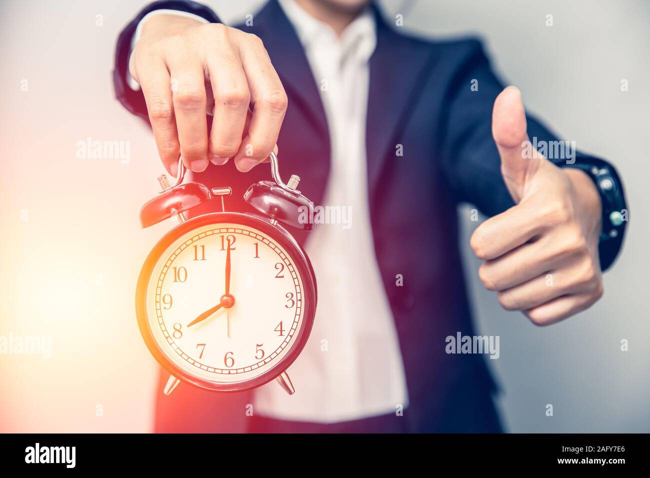 Business person hand showing thumbs up with a clock for good times or right time work on time concept. Stock Photo