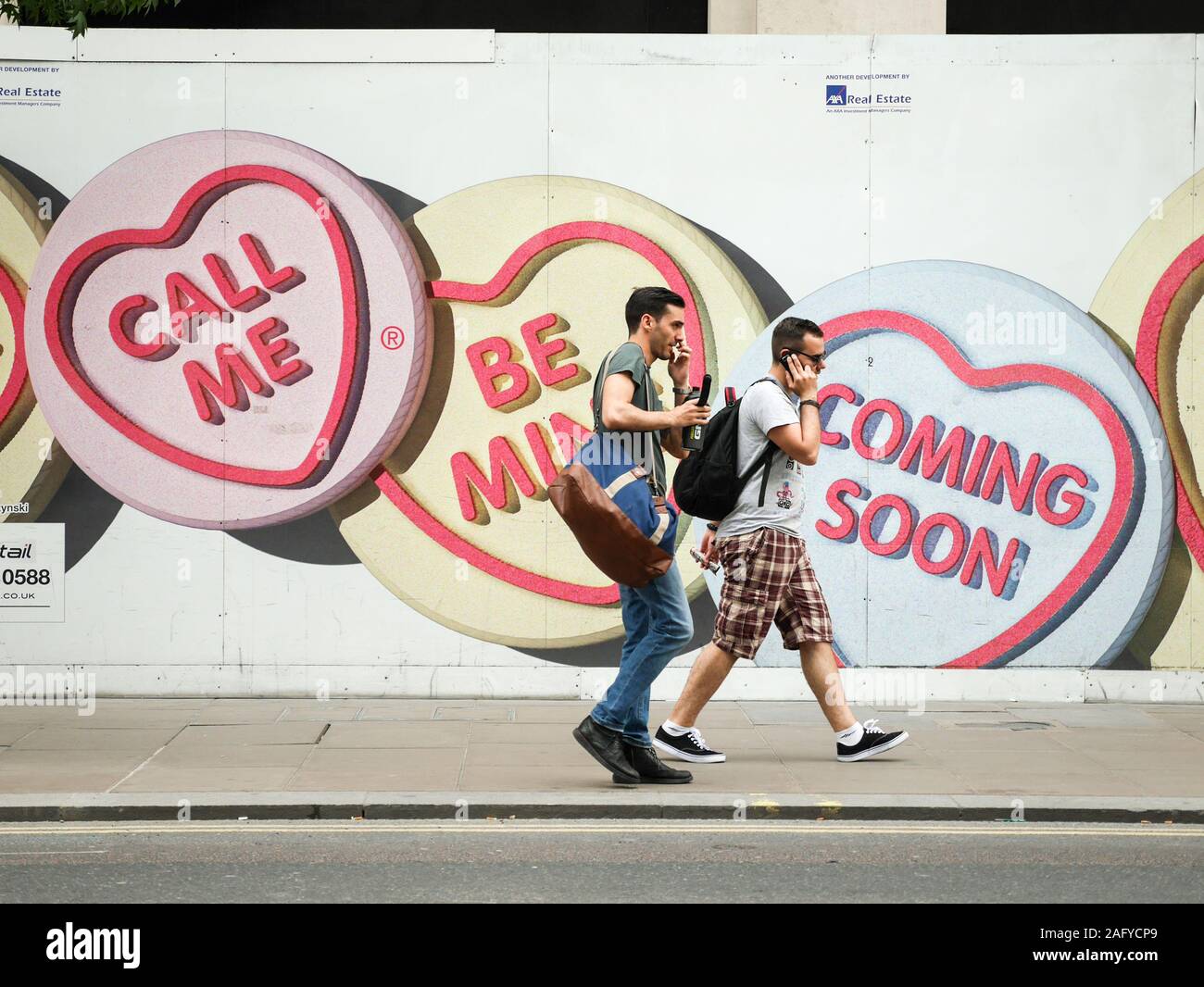 Love Hearts: Call Me. Pedestrians on mobile phones walking by advertising for Love Hearts, a UK sweet brand, with the slogan 'Call Me'. Stock Photo