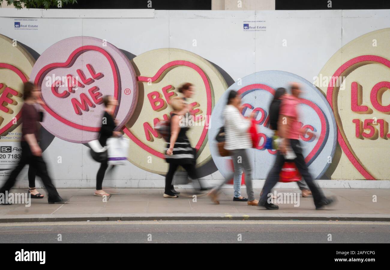 Love Hearts. Anonymous motion blurred pedestrians walking by advertising hoarding for Love Hearts, a popular UK sweet brand. Stock Photo