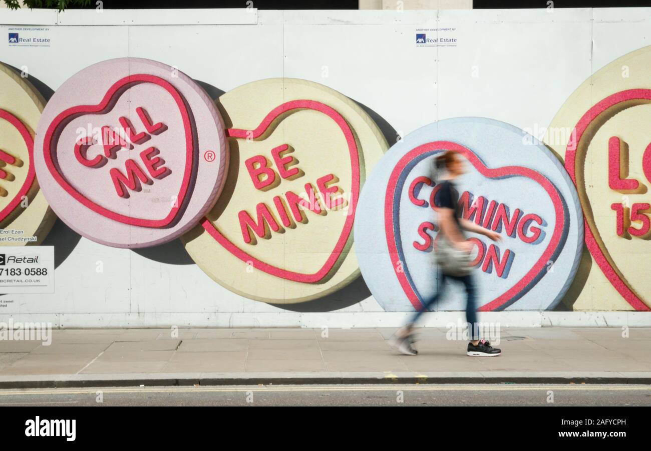 Love Hearts: Be Mine. Motion blurred pedestrian walking by advertising hoarding for Love Hearts, a popular UK sweet brand. Stock Photo