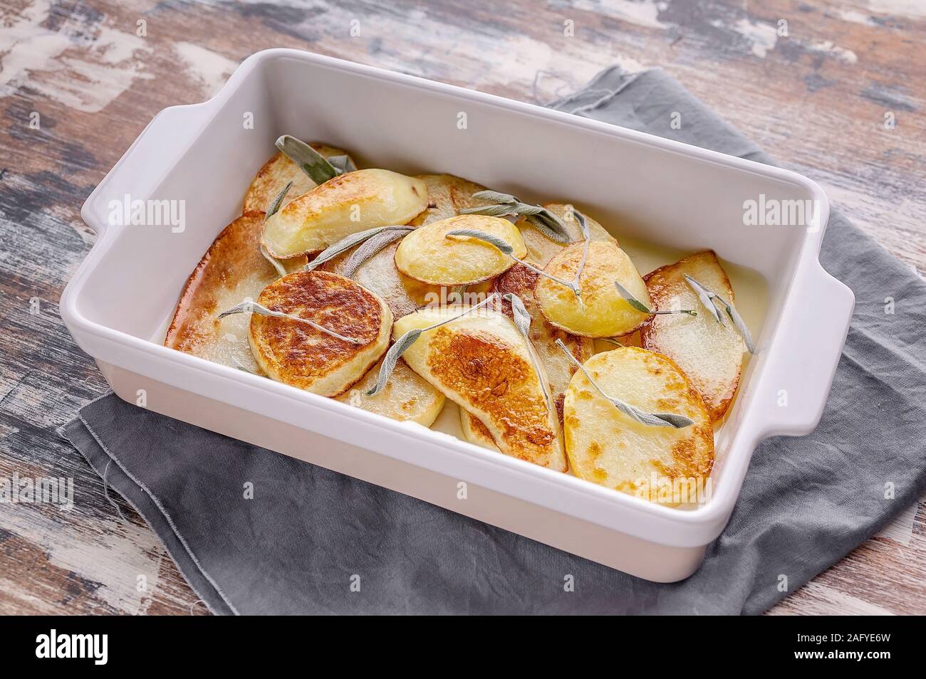 Closeup baked sliced potato with red onion and herbs: sage, rosemary and thyme in a ceramic baking dish. Stock Photo