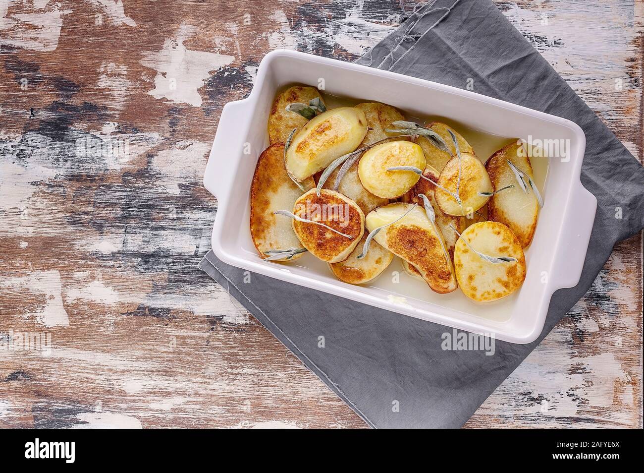 Baked sliced potato with red onion and herbs: sage, rosemary and thyme in a ceramic baking dish. Top view. Copy space Stock Photo