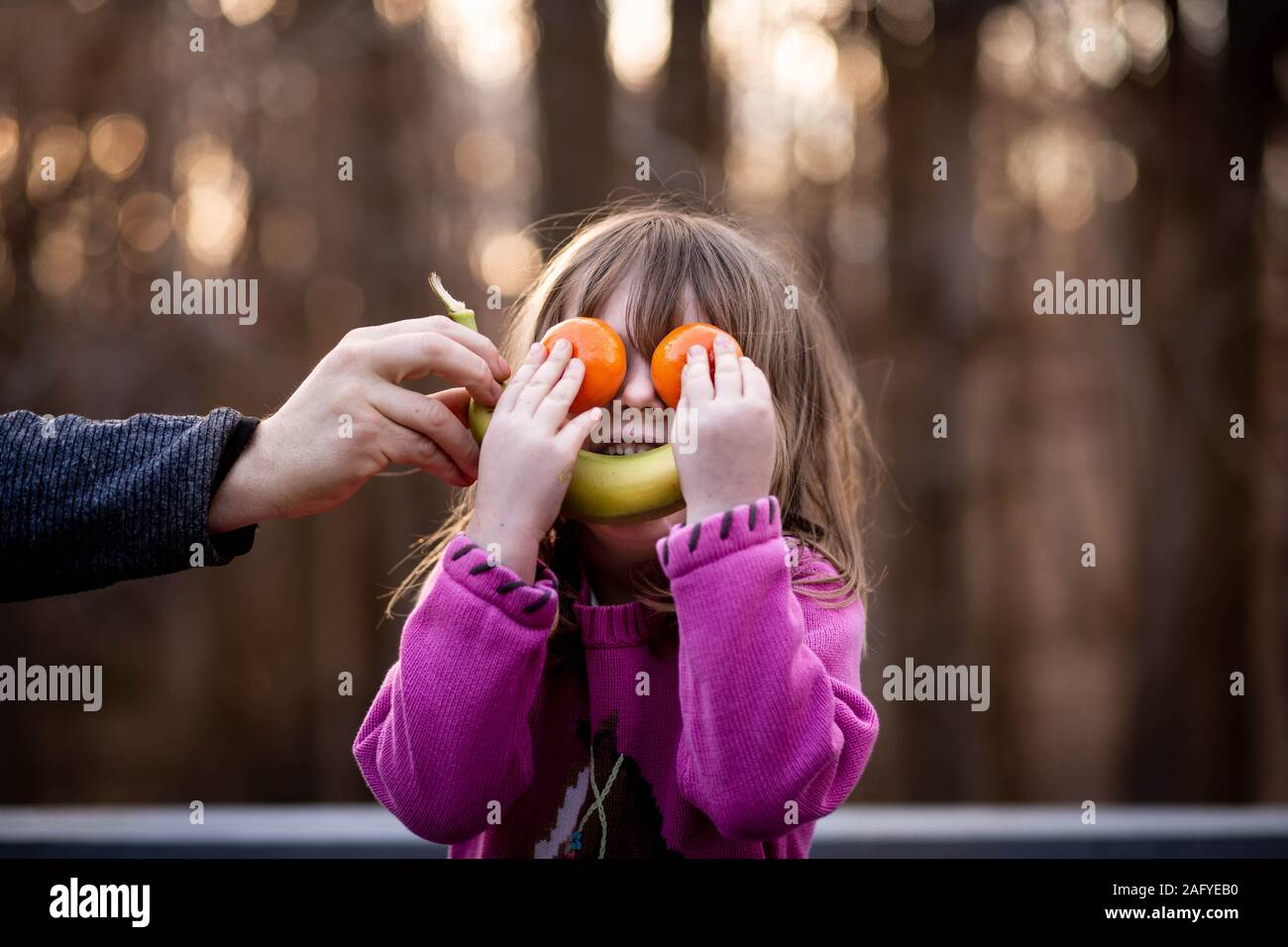 young girl puts fruit on face to make silly face outside Stock Photo