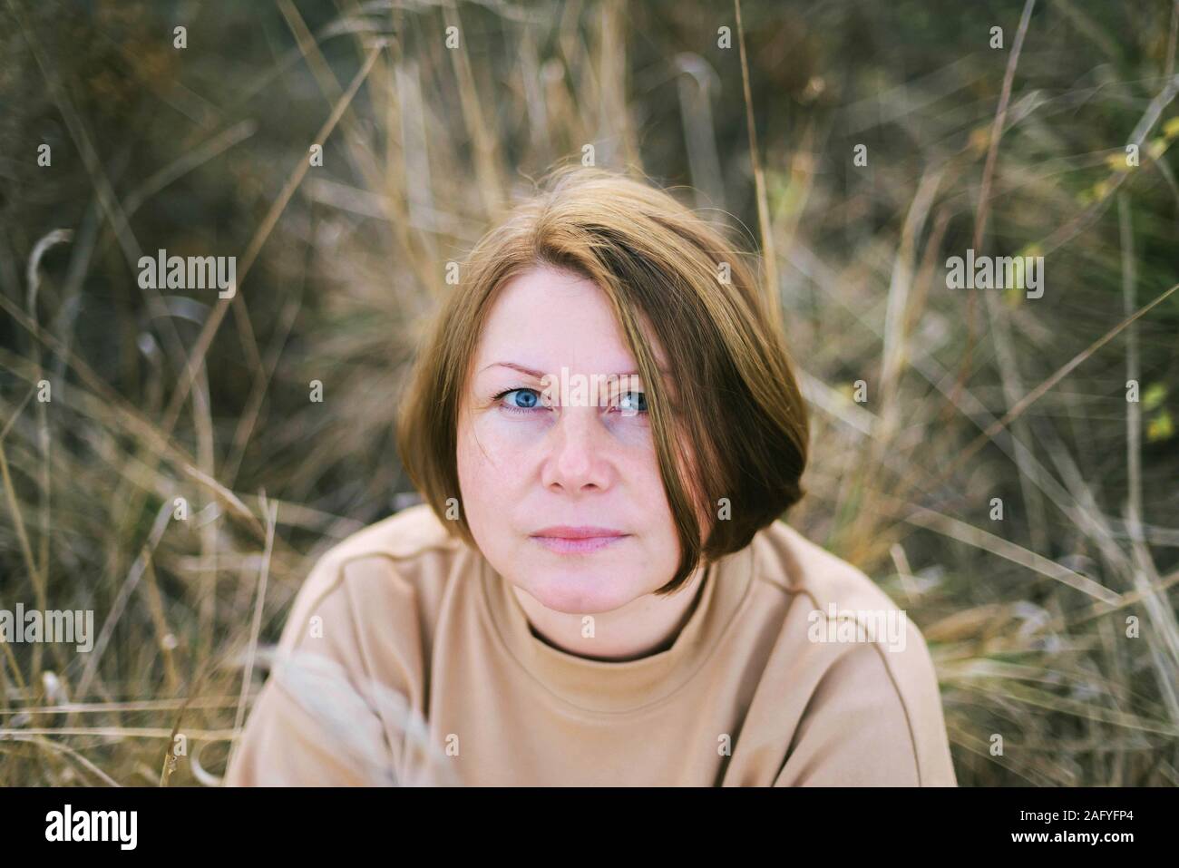 portrait-of-a-40-years-old-woman-sitting-on-dry-grass-outdoors-stock