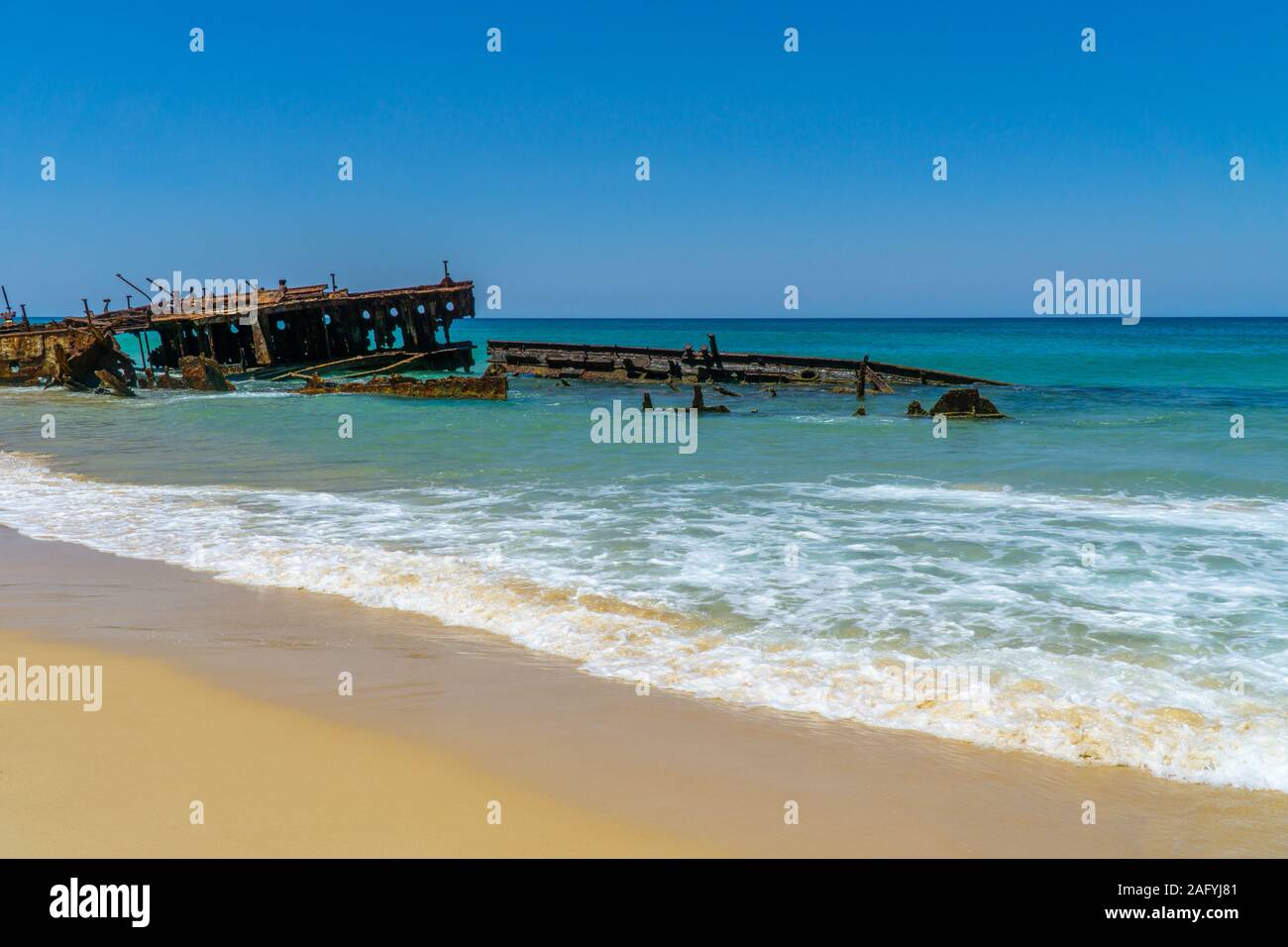 on the beach of fraser island lies the skeleton of a washed-up shipwreck in fine weather Stock Photo