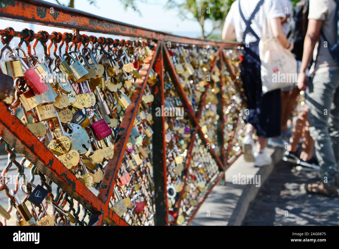 PARIS, FRANCE - SEPTEMBER 16, 2019: Numerous padlocks and combination locks fixed to the fence at the Sacre Coeur in Paris. Tourists lean on the fence Stock Photo