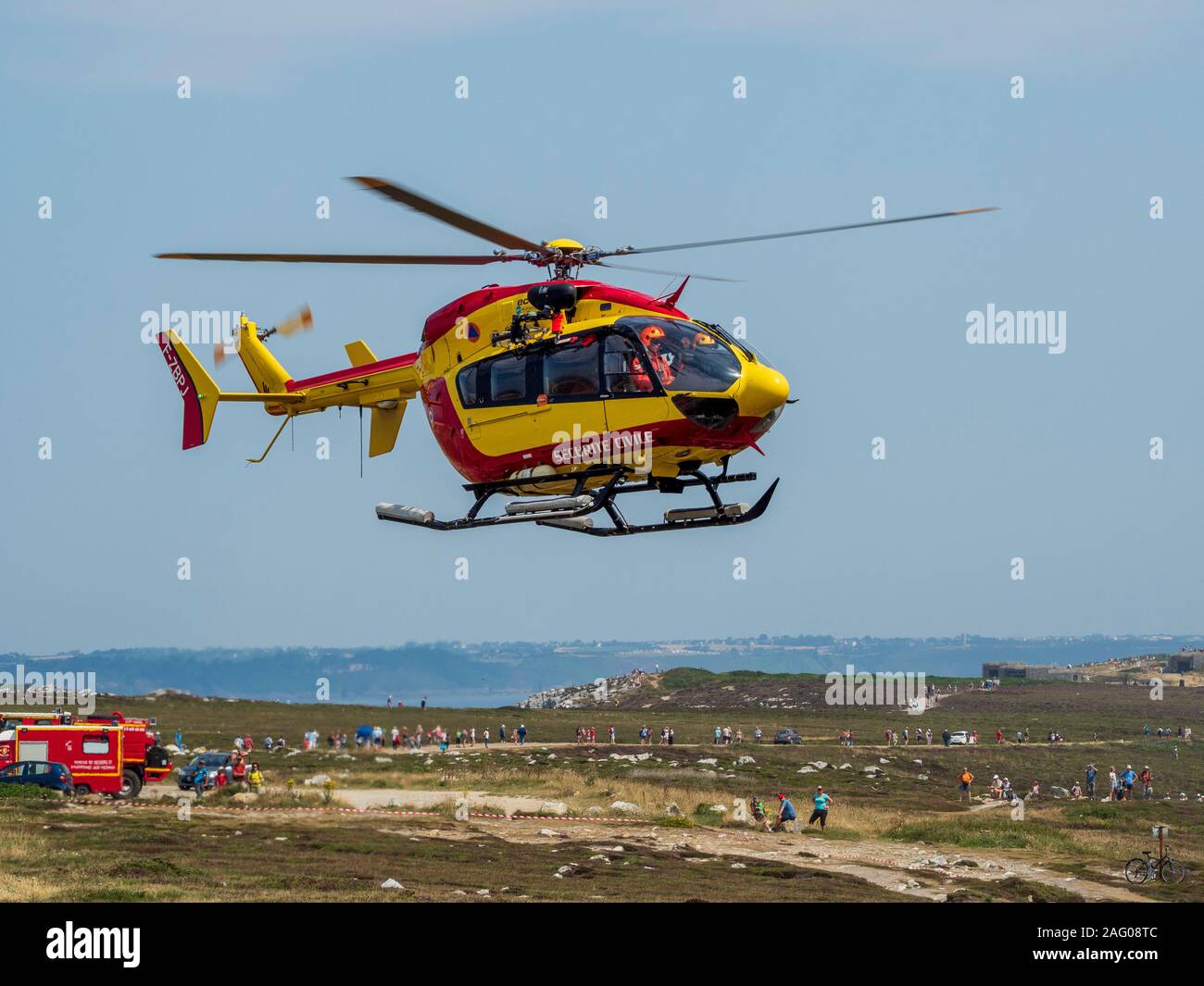 Civil Protection helicopter taking off with fire engines in the background. France. Stock Photo