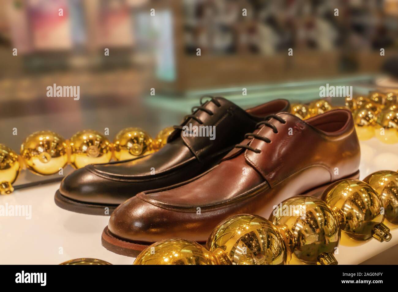 two men's shoes, black and brown, in the window of a Shoe store, decorated with yellow Christmas balls. Stock Photo