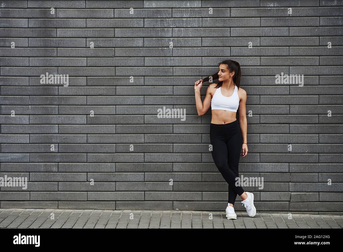 Young sportive brunette with slim body shape against brick wall in the city at daytime Stock Photo