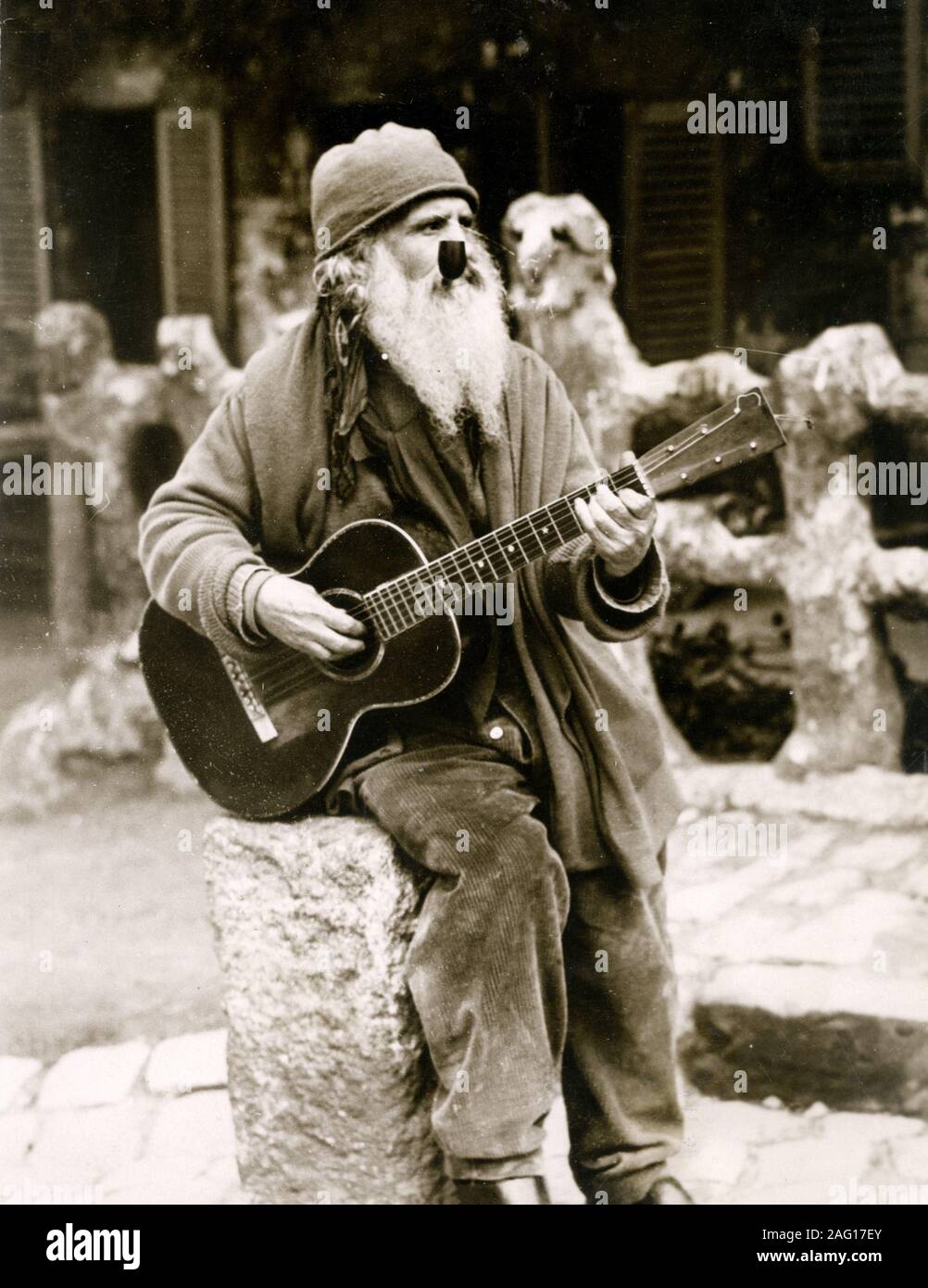 Early 20th century vintage press photograph - old musician with guitar and pipe playing music outside the Lapin Agile club in Montmartre Paris, c.1920s Stock Photo