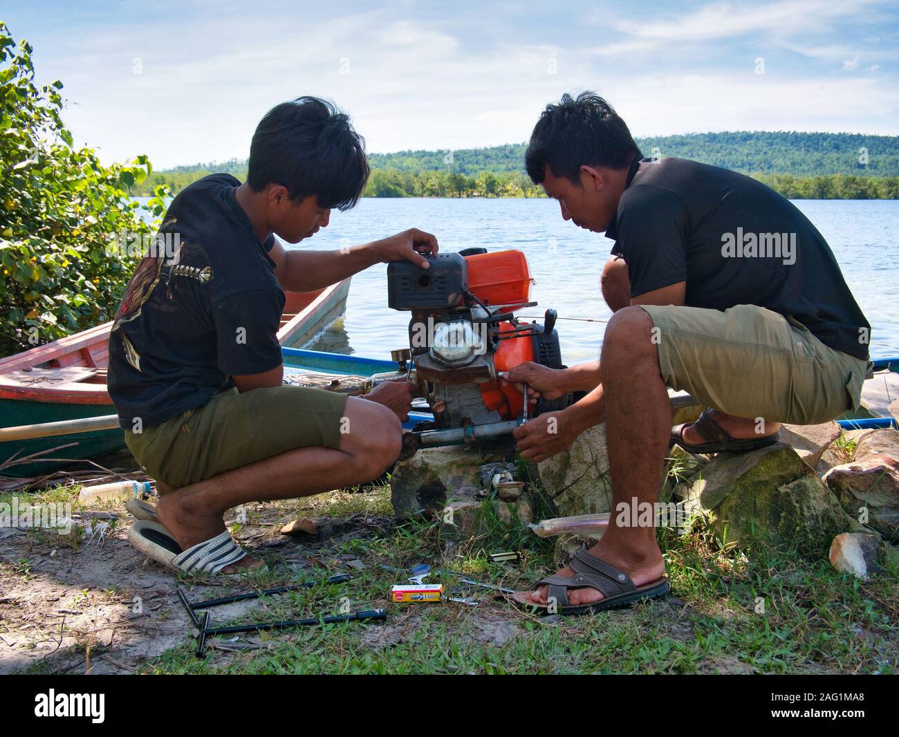 Two young men repair a longtail outboard motor in a remote rural village in Koh Kong Province in Cambodia. Stock Photo