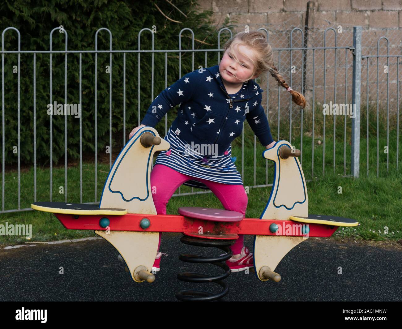 Young girl with pigtails, plaited hair, in a park playground playing on a sea saw. Stock Photo