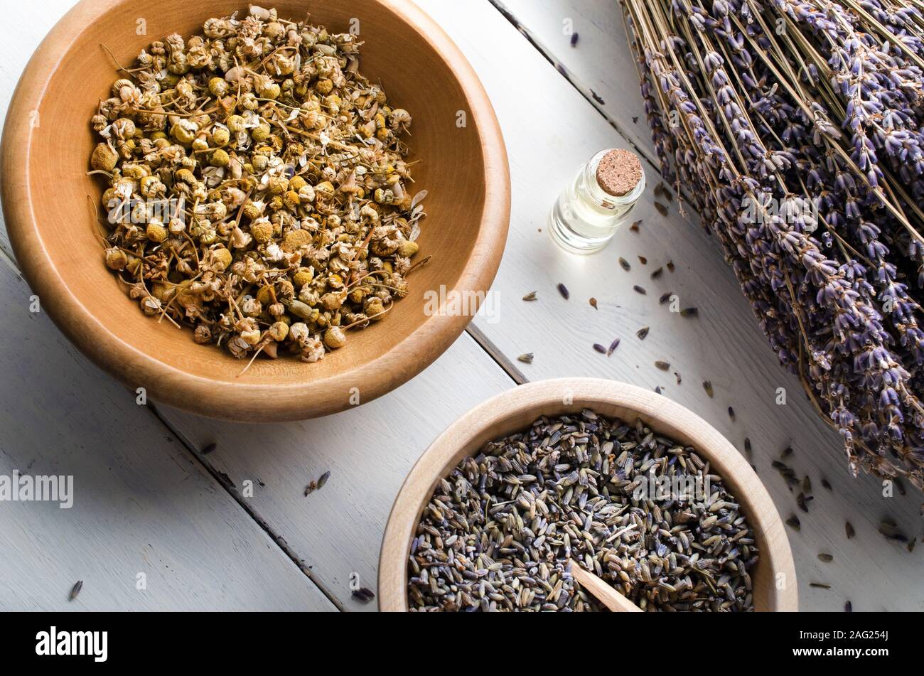 Angled overhead shot of dried herbs and essential oil. Includes wooden bowls of chamomile and lavender with a tied bunch of stemmed flowers to the sid Stock Photo