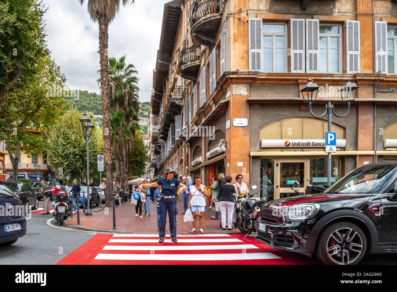 A female policewoman directs traffic at a red and white crosswalk in the urban center of Ventimiglia, on the Italian Riviera. Stock Photo
