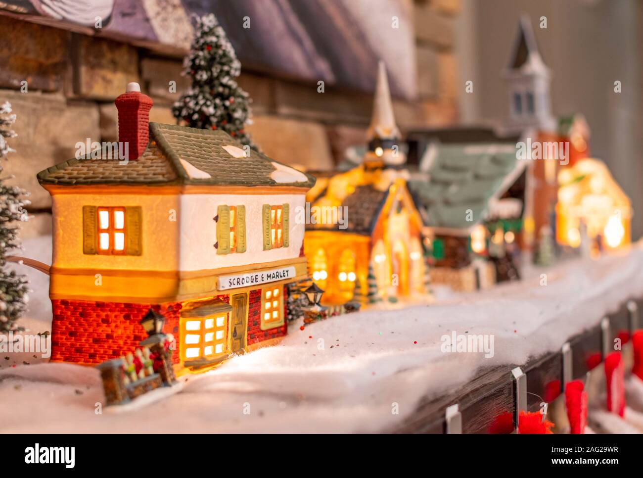 A miniature, illuminated Victorian Christmas village of shops and businesses, including a Scrooge and Marley building, on a mantel during the holidays Stock Photo