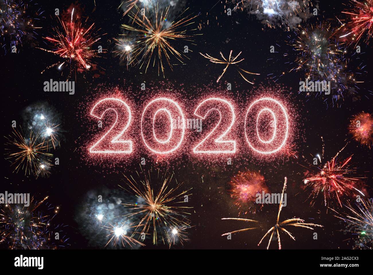 2020 year written with sparkle fireworks on night sky, surrounded by fireworks of different colors. Happy New Year 2020 greeting concept Stock Photo