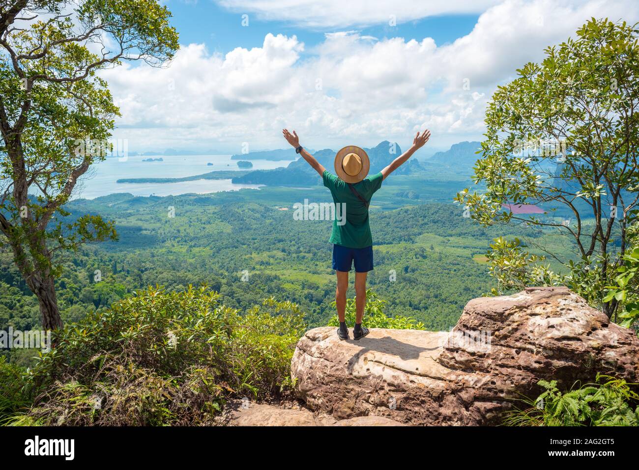 Stock image: young man with hands stretched up stands on rock high in mountains. Concept of success, healthy lifestyle, harmony, travel on vacation. Stock Photo