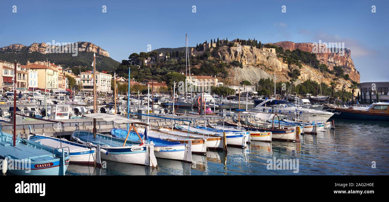 Boats docked in a quay of Cassis port town in Southern France. Panoramic scenery. Château de Cassis and cliffs of Cap Canaille in the background. Cass Stock Photo