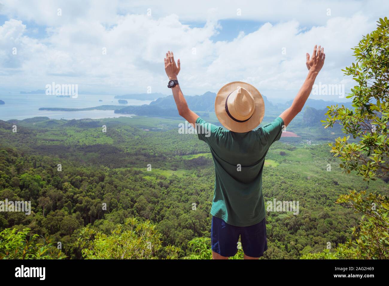 Stock image: a happy traveler with his hands raised up in admiration stands on top of high mountain and watches landscape of forest, hills, and sea. Stock Photo