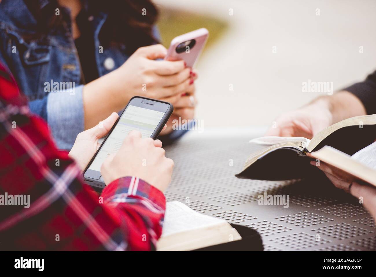 Closeup shot of females using their smartphone while reading the bible Stock Photo