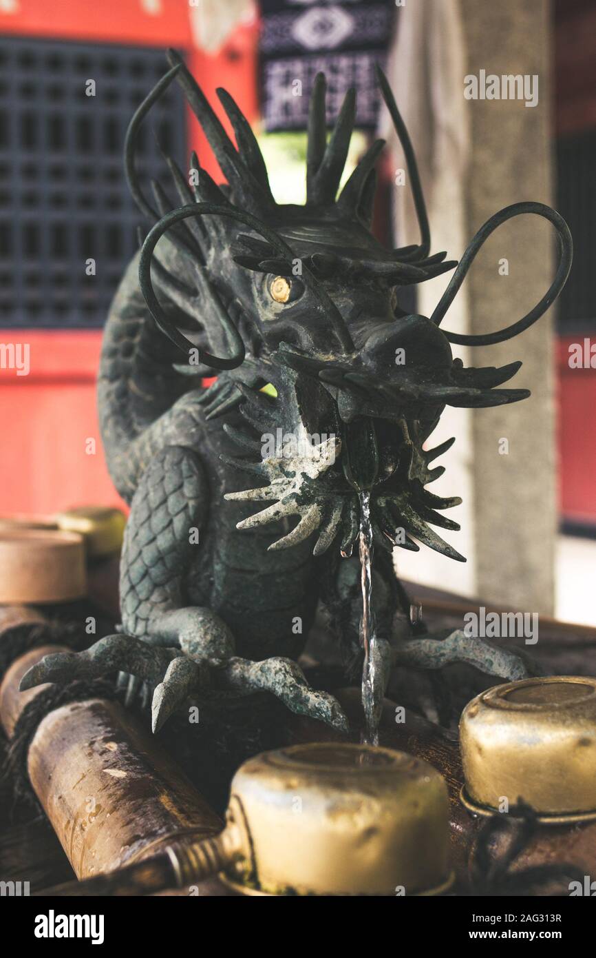 Vertical shot of a black dragon statue with shiny eyes and water coming out of its mouth Stock Photo