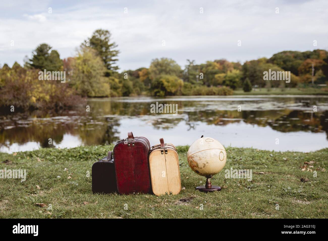Closeup shot of old suitcases on a grassy field near desk globe with blurred water in background Stock Photo